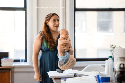 Cindy holding a demo doll, she is smiling and speaking to students at either a doula training.  nj birth class morristown birth class nj doula services, birth doula morristown hospital