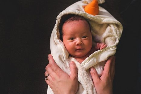 picture of persons hands on smiling baby who is wrapped in a white snowman blanket.  hackettstown birth doula services.  morristown birth doula services.  saint clare's hospital birth doula